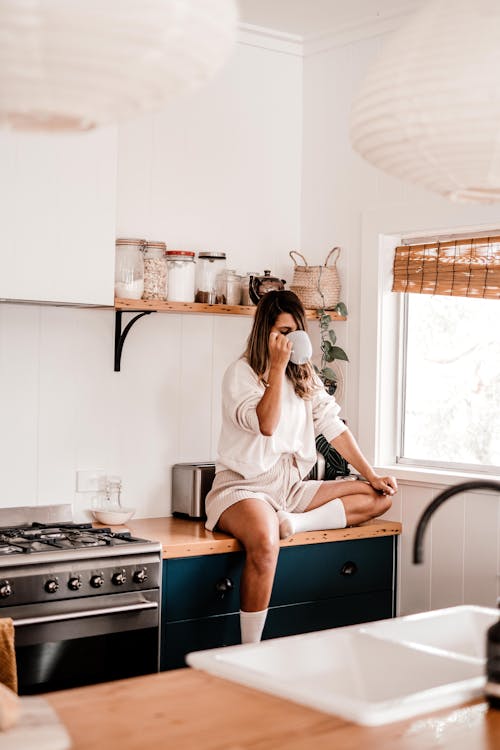 A Woman Drinking while Sitting on the Kitchen Counter