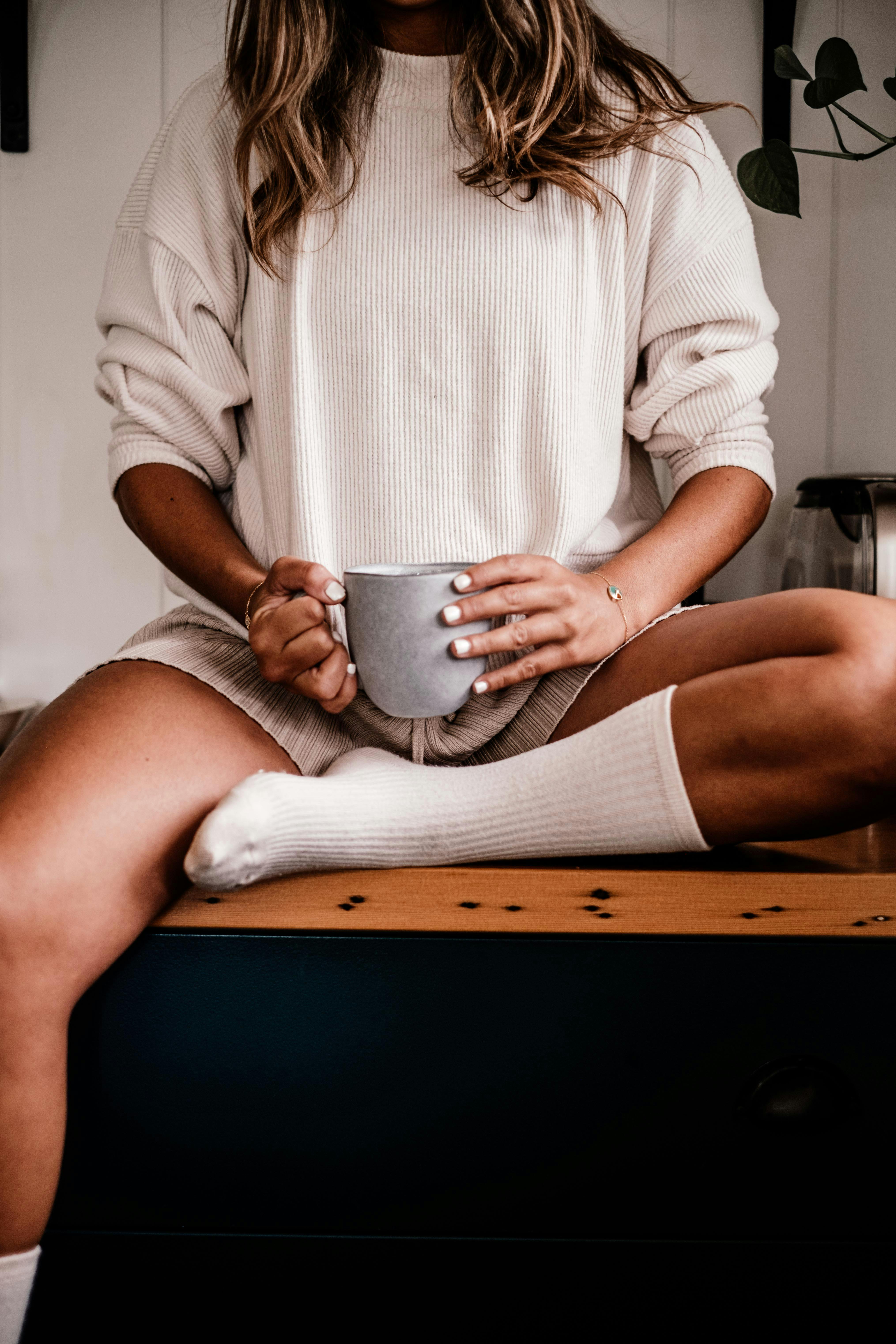 Woman enjoying a cozy morning indoors with a coffee mug, dressed in comfortable home wear.