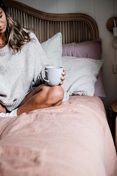 Free Woman sitting on bed with a mug, embracing a cozy and relaxed morning atmosphere. Stock Photo