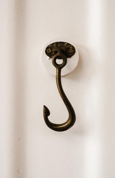 Close-up of a vintage brass hook mounted on a white wall, highlighting texture and detail.