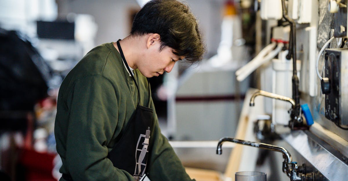 An Asian man wearing an apron works diligently in an industrial kitchen setting.