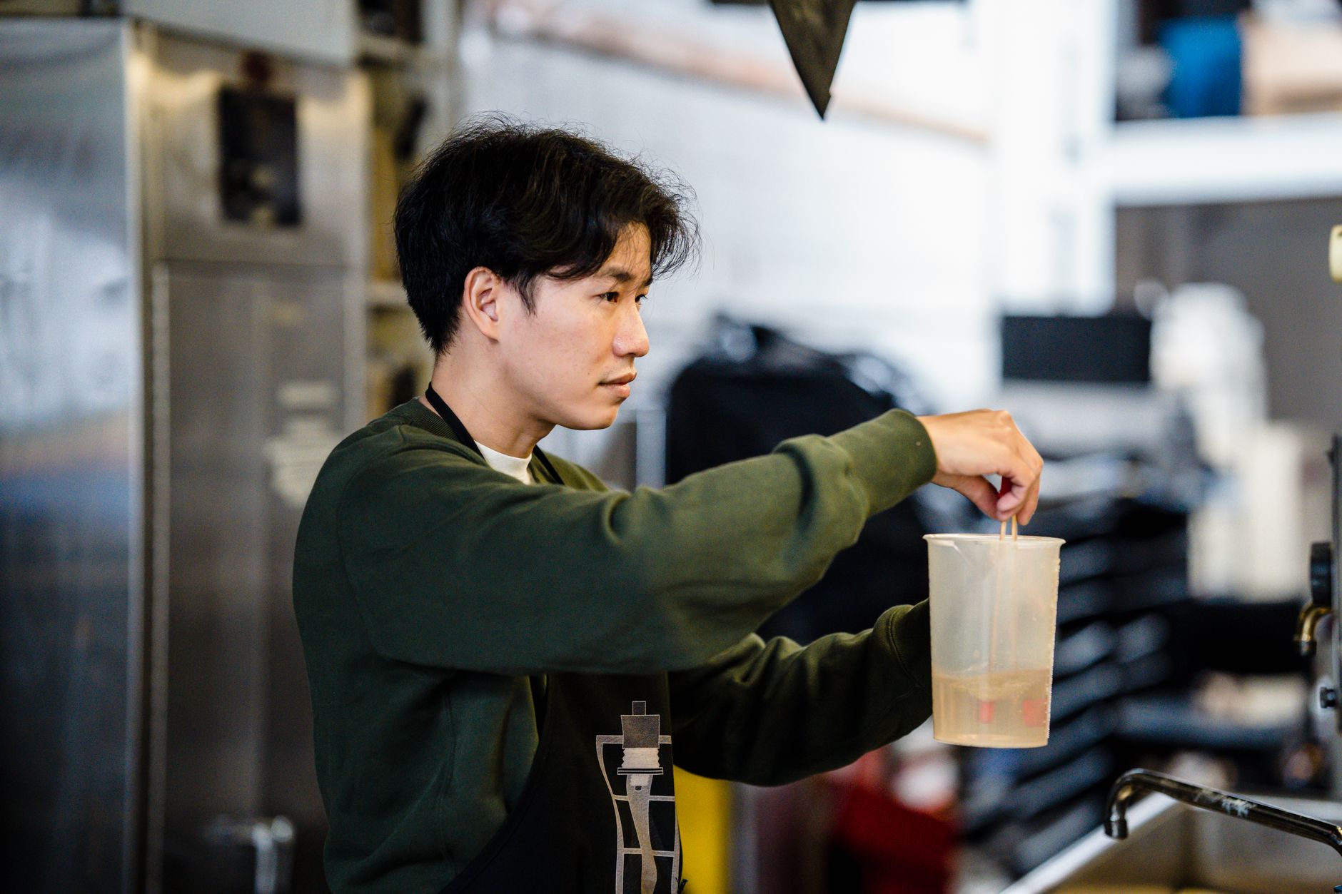 Asian man stirring liquid in a large measuring cup in a kitchen setting.