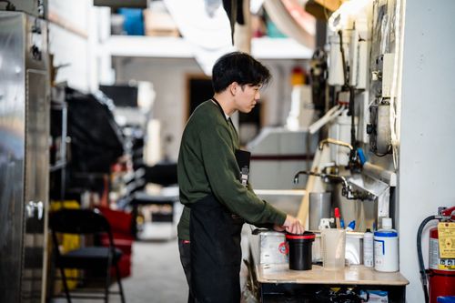 Free Asian man in green sweater mixing chemicals in an industrial workspace indoors, focused on work. Stock Photo