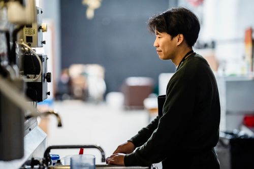 Free Asian man focused on work in a modern industrial workspace. Ideal for business and technology themes. Stock Photo