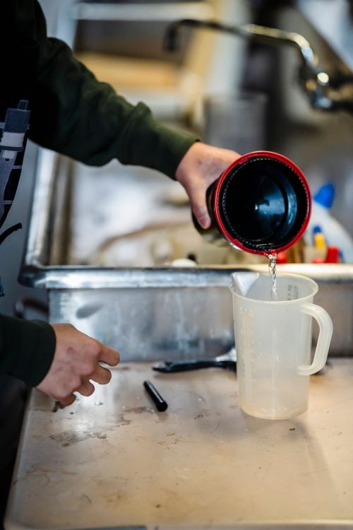 Free Close-up of a person pouring liquid from a container into a white measuring jug in a kitchen sink. Stock Photo