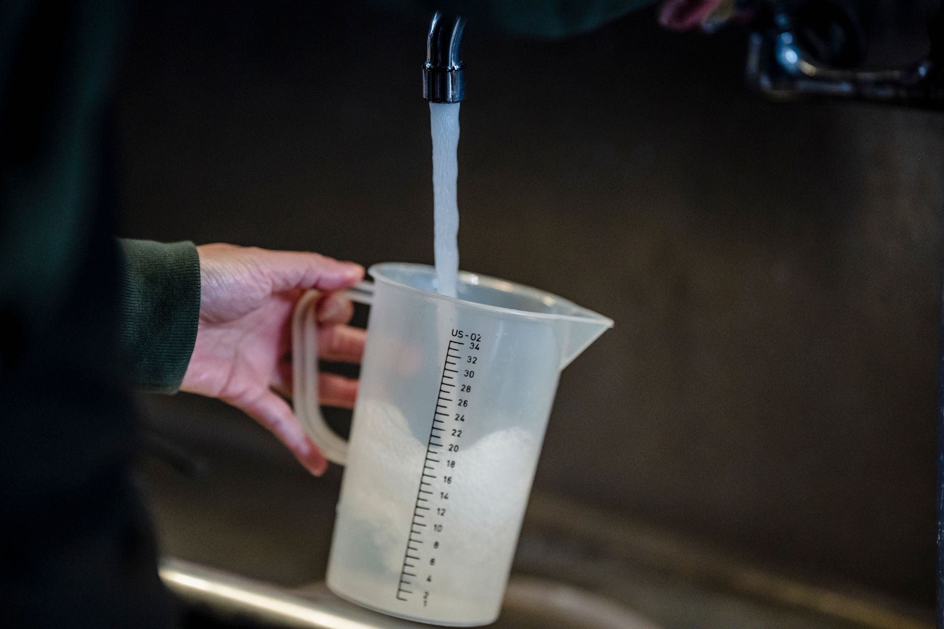 Close-up of hand holding measuring pitcher under a faucet with running water indoors.