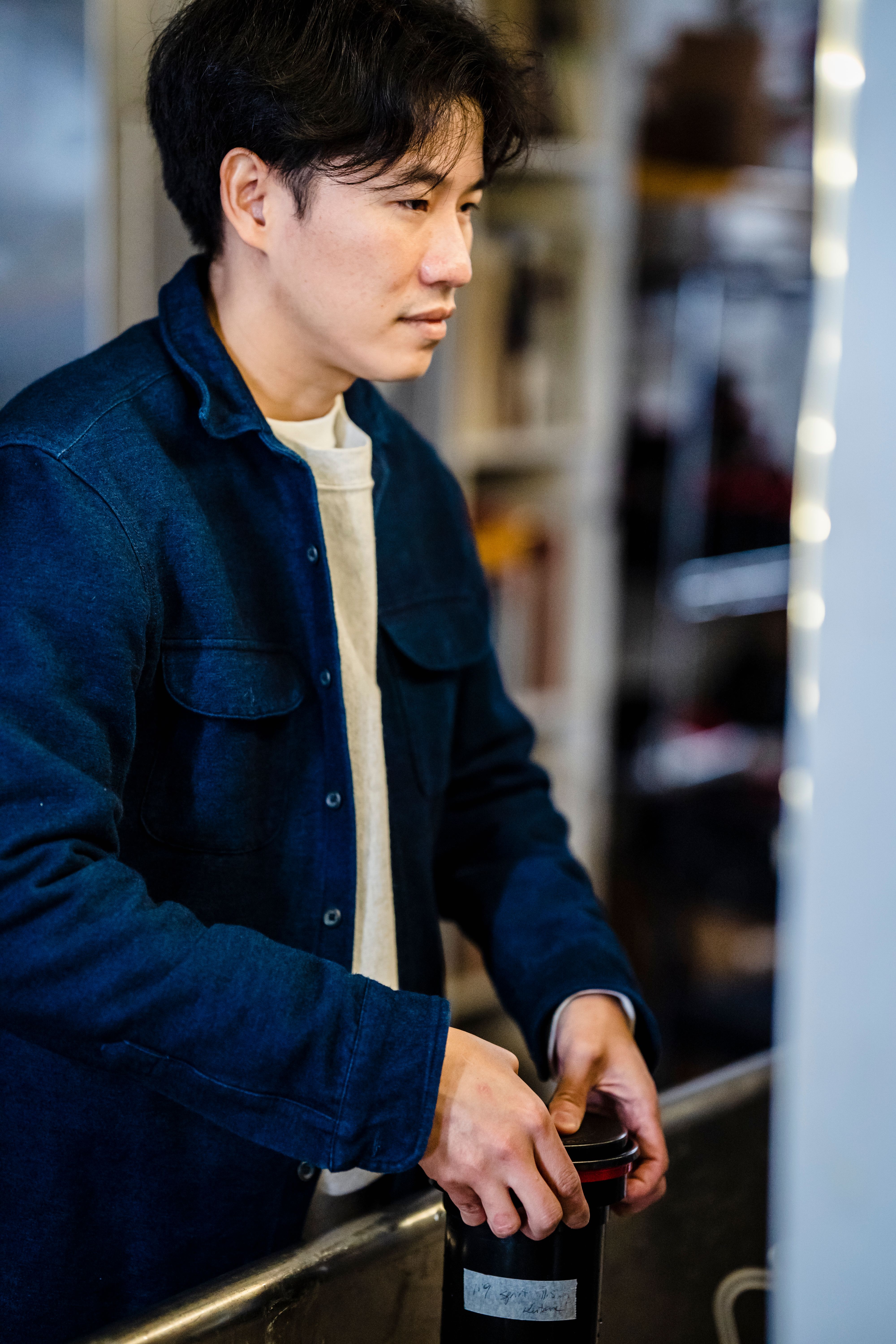 Man in a blue jacket holding camera equipment indoors, focusing on his task.