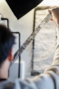 Person holding and examining black-and-white film negative in indoor setting.