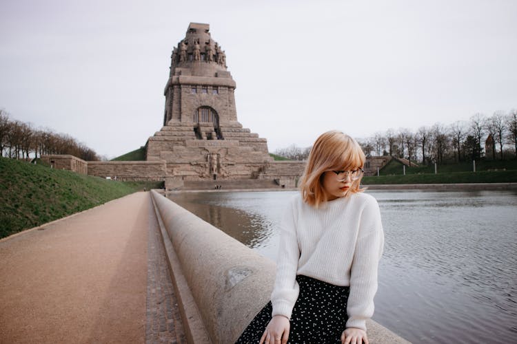 Young Woman Sitting On A Wall In Front Of The Monument To The Battle Of The Nations