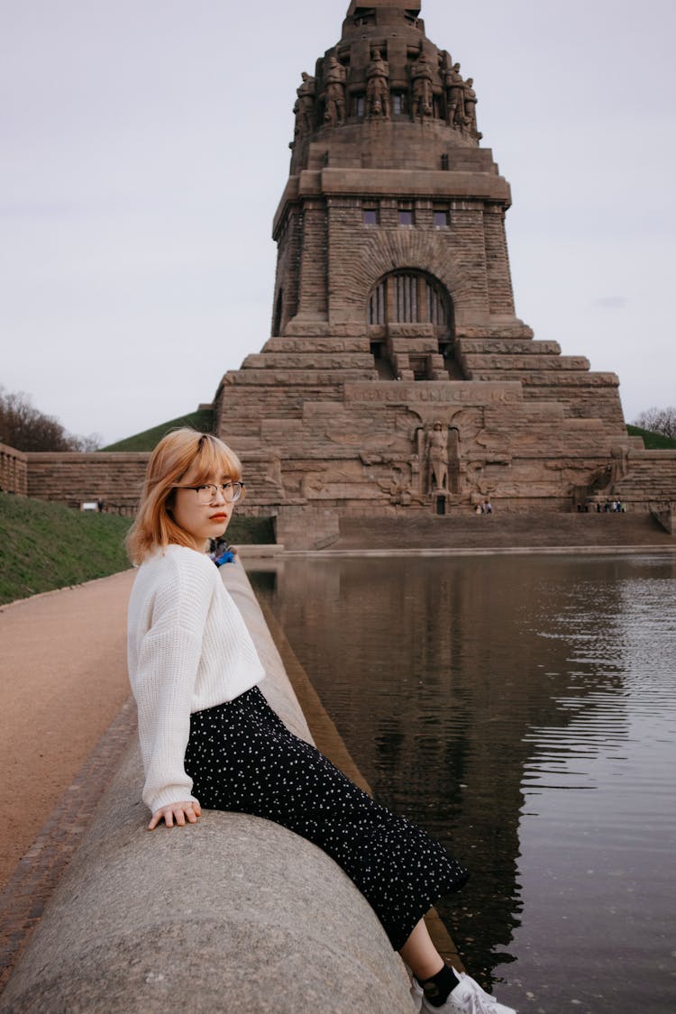 Young Woman Sitting On A Wall In Front Of The Monument To The Battle Of The Nations