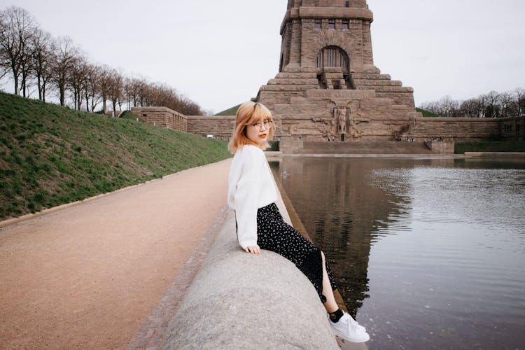 Young Woman Sitting On A Wall In Front Of The Monument To The Battle Of The Nations