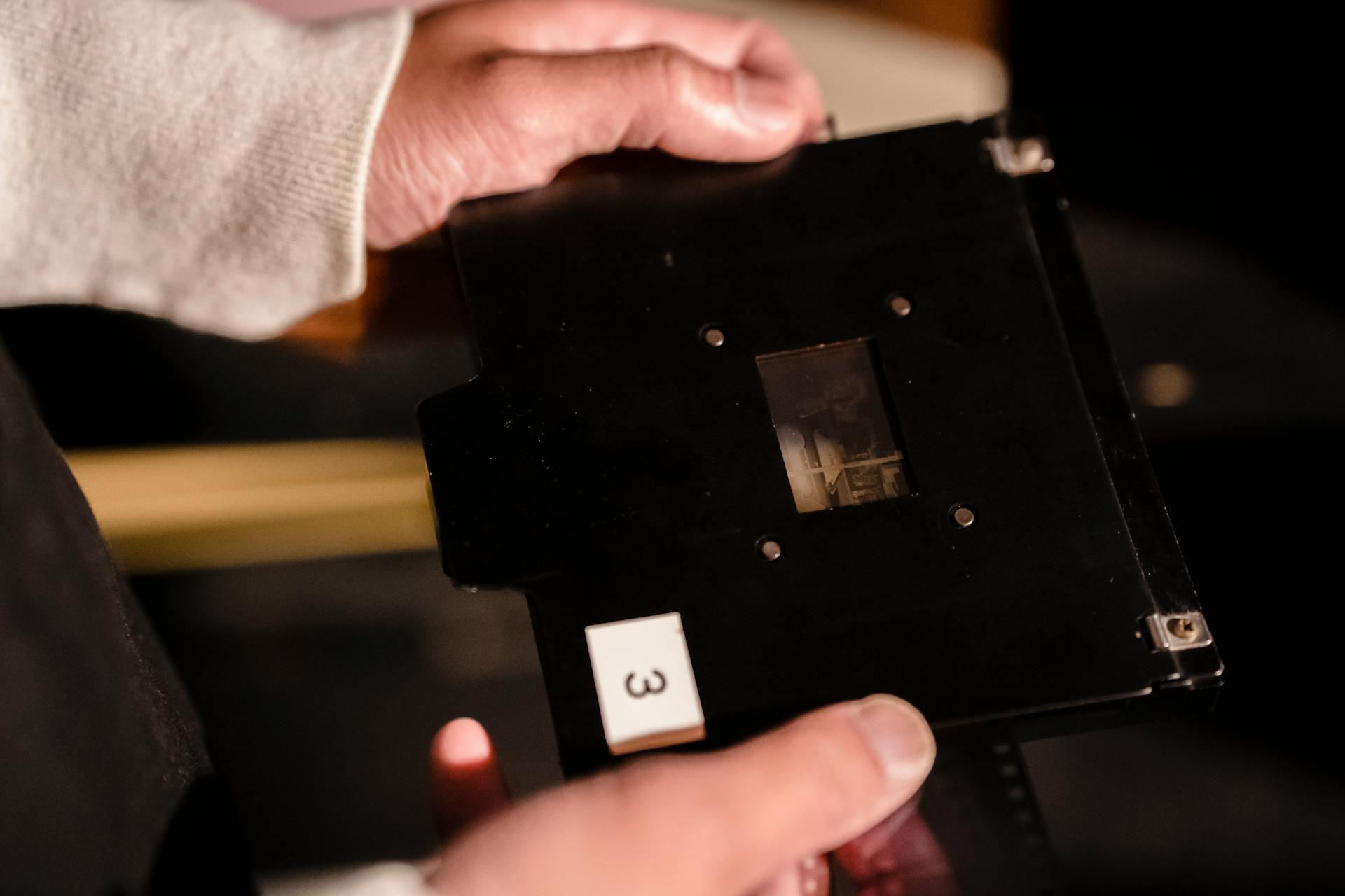 A hand holds a black film slide showing a processed image in a darkroom setting.