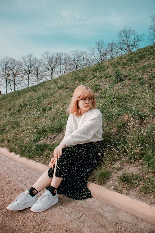 Young Woman Sitting on Grass on the Side of a Pavement 