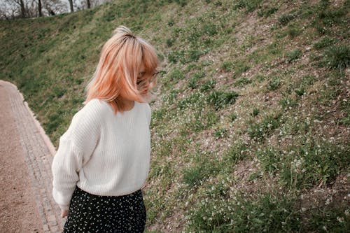 A Woman in White Sweater Standing on Green Grass Field