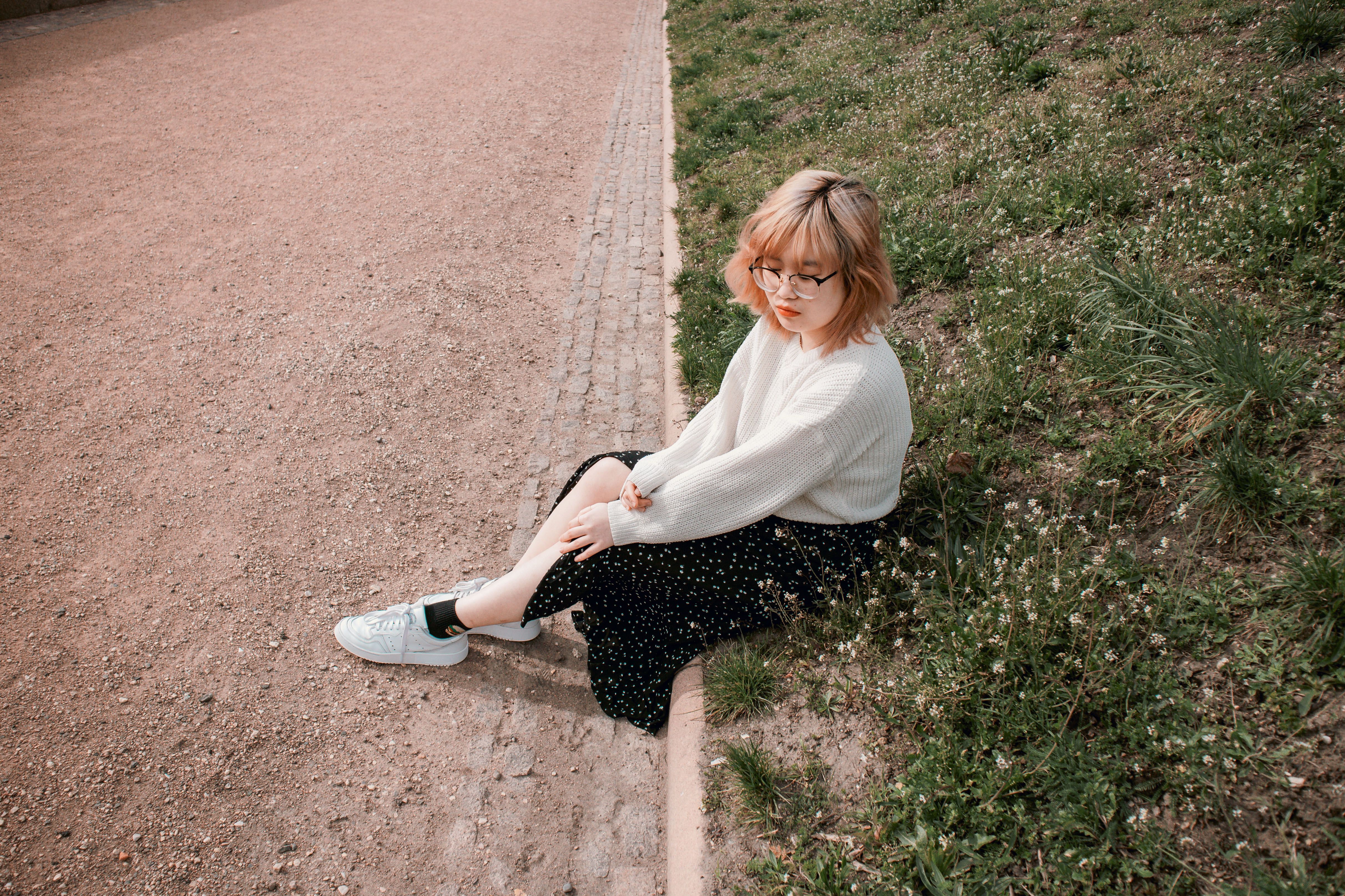 A Woman in Knitted White Sweater Sitting on Green Grass Field · Free ...