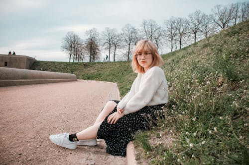 Young Woman Sitting on Grass on the Side of a Pavement 