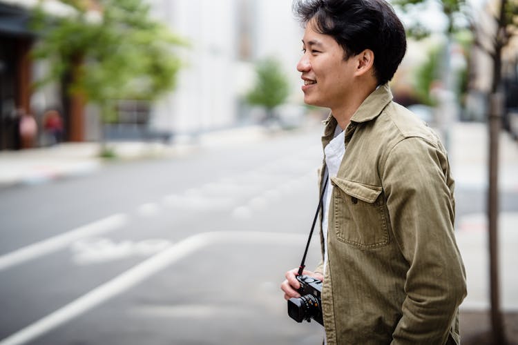 Smiling Man With A Camera Hung On His Neck In City 