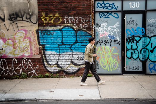 Man walking past a vibrant graffiti wall in the city, reflecting urban culture.