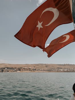 Turkish flags flying over the serene waters of Lake Van with scenic hills in the background.