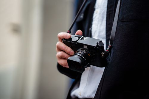 Free Person holding a camera with a strap, focusing on photography equipment. Stock Photo