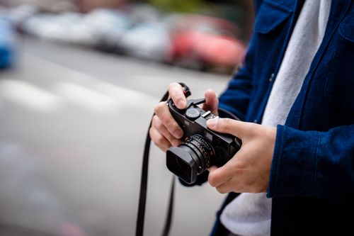 Free A close-up view of hands holding a camera on an urban street. Stock Photo