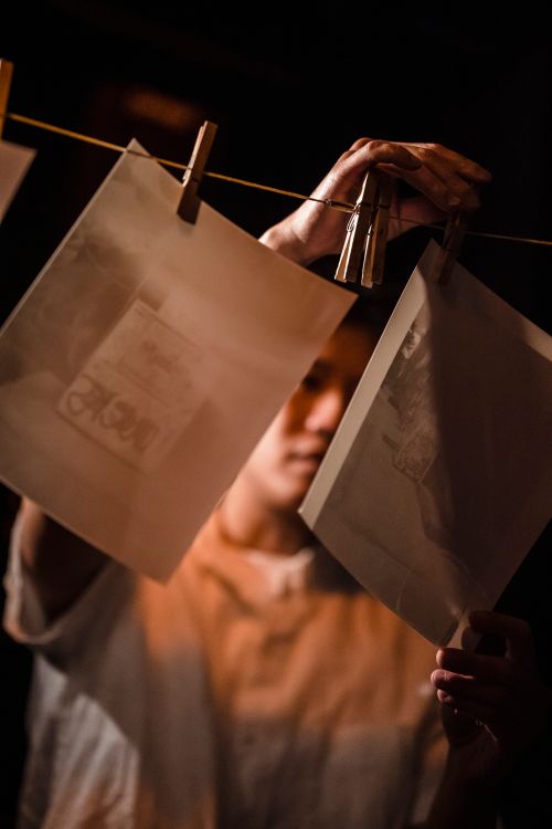 Free A person hanging photo prints on a line in a darkroom with warm lighting. Stock Photo
