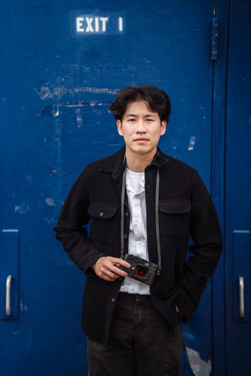 Free Portrait of a male photographer with a camera against a blue door, urban background. Stock Photo