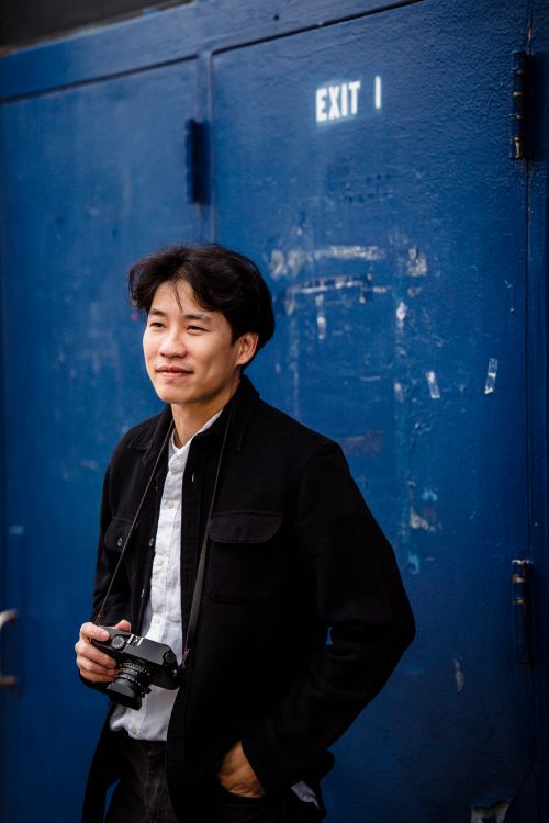 Free Young photographer smiling and holding a camera against a blue wall. Stock Photo