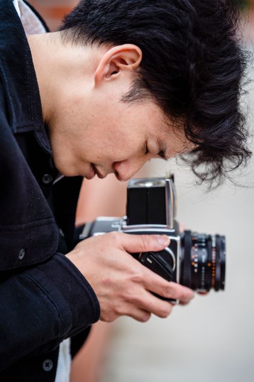 Free Close-up of an adult photographer concentrating while using a vintage camera outside. Stock Photo