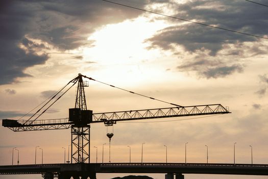 A dramatic silhouette of a tower crane against a sunset sky, representing construction and industry.