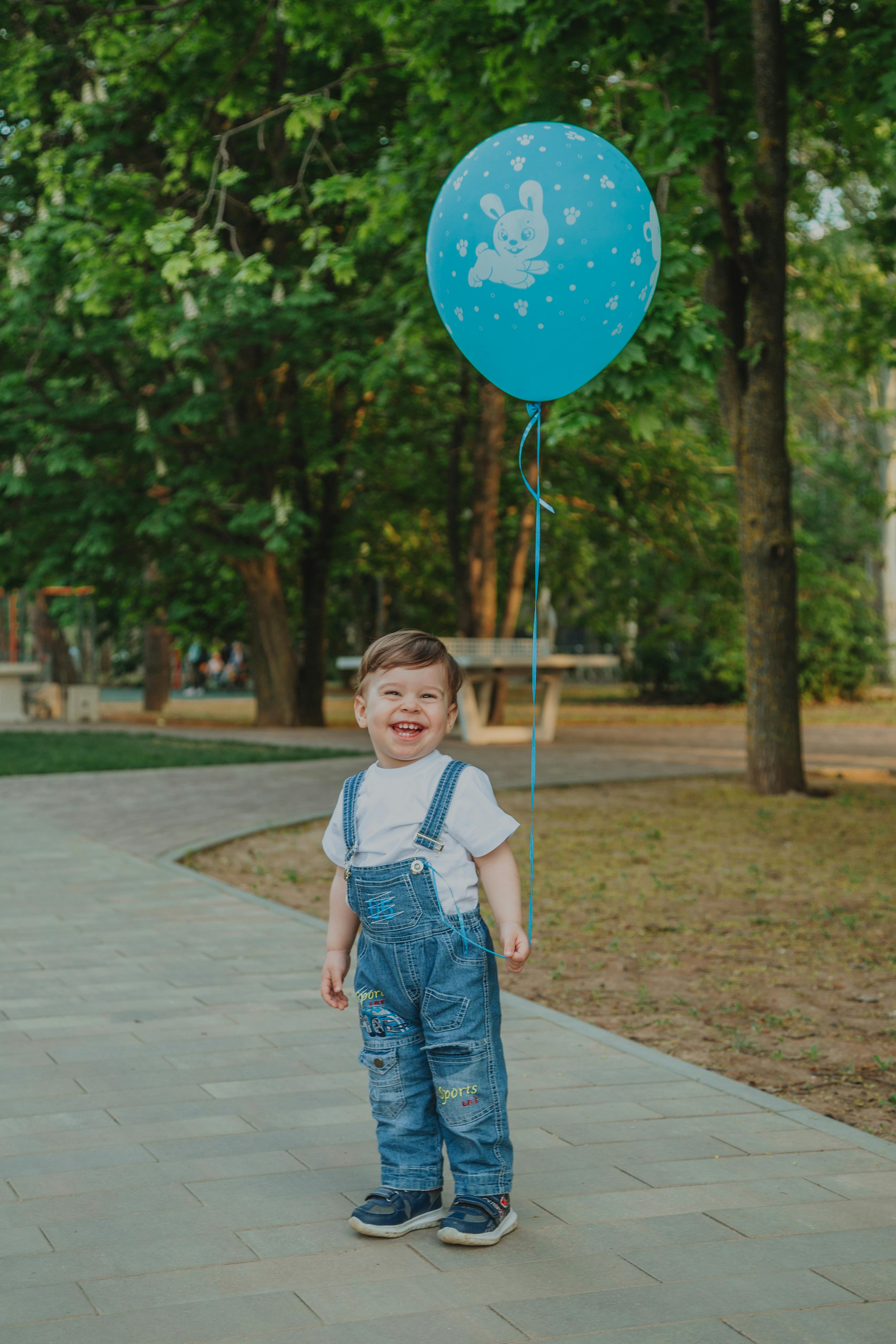 positive boy with balloon on footpath in park