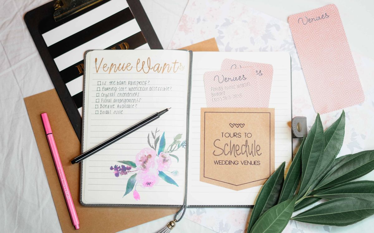 Flat lay of wedding planning materials including a journal, leaves, and stationery.