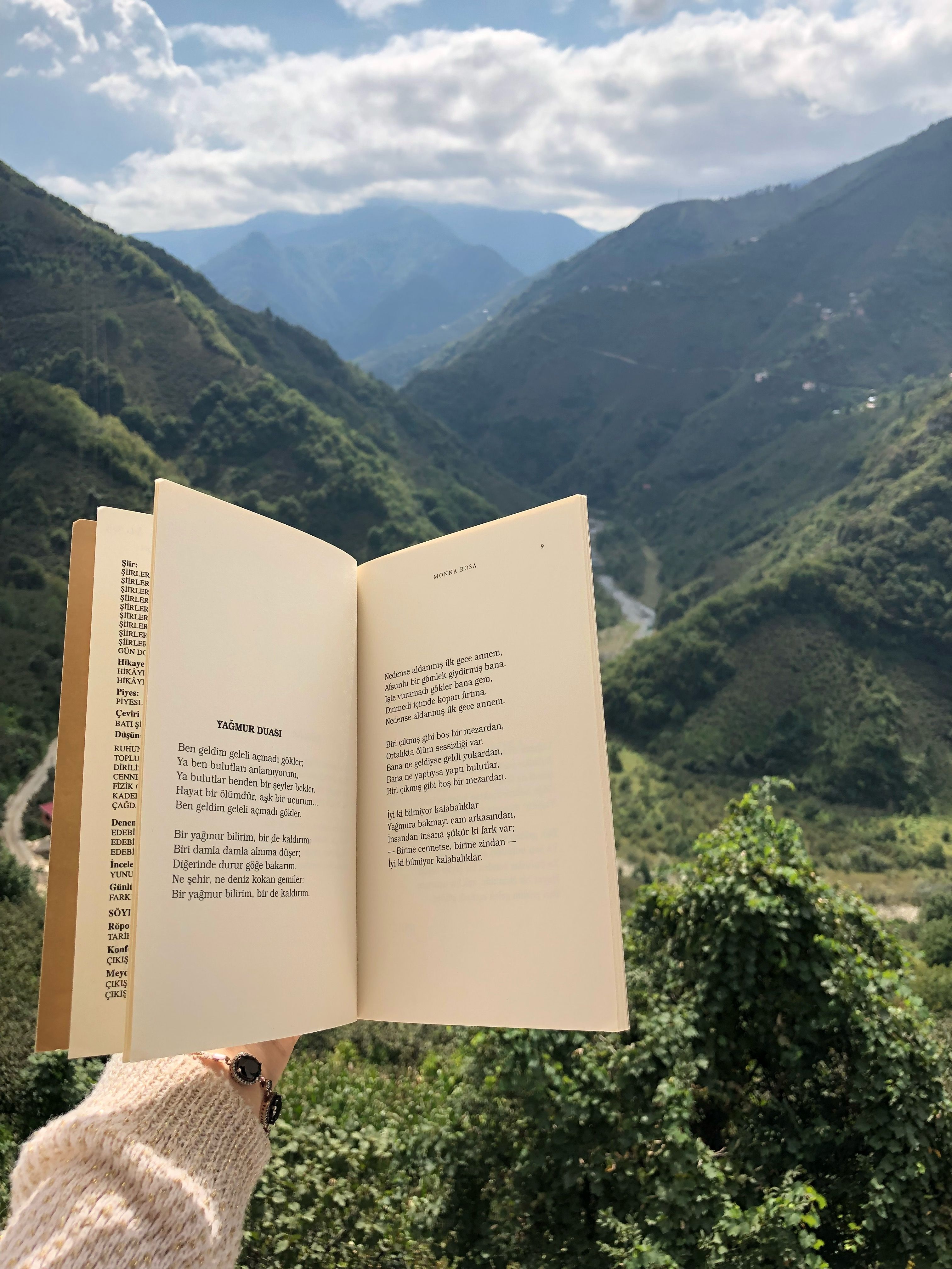 Person holding a book against a stunning background of Giresun mountains under a bright sky.