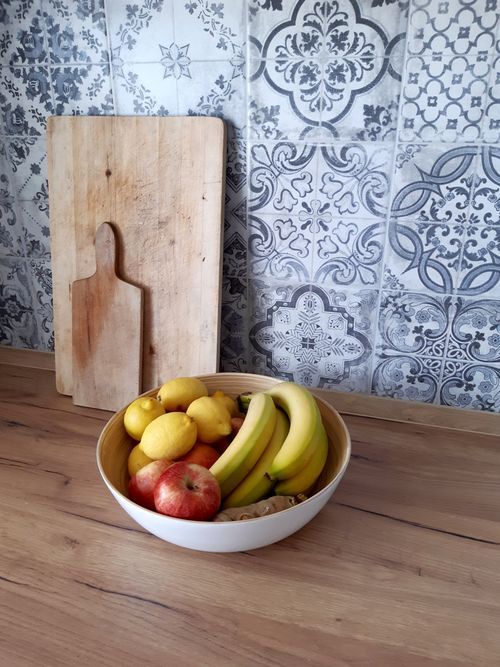 Free A bowl of bananas, lemons, and apples on a wooden kitchen countertop with decorative tiles. Stock Photo
