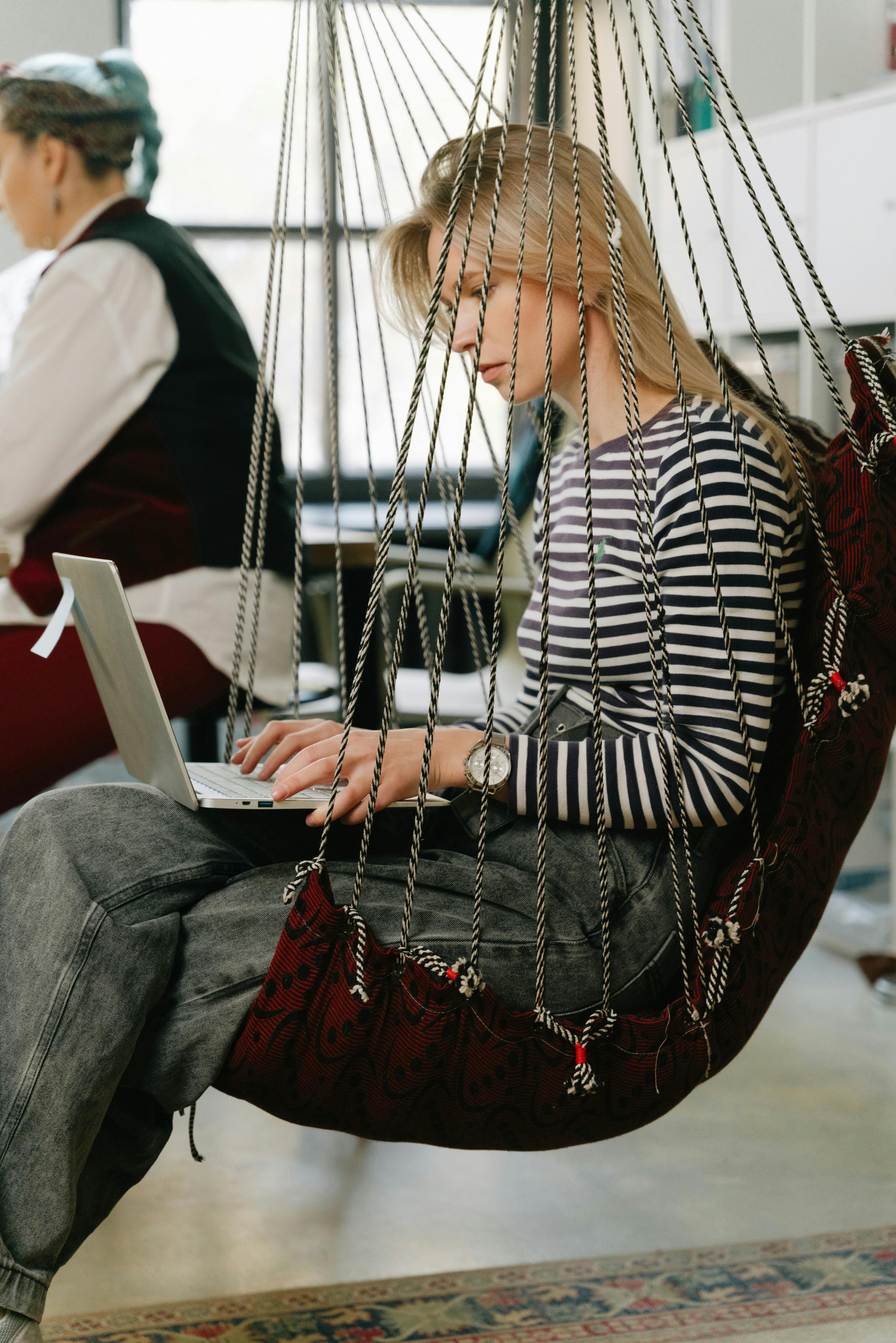 Focused woman working on a laptop while seated in a cozy indoor hammock.