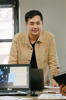 Asian professional in a brown jacket discussing business strategies at an office meeting.
