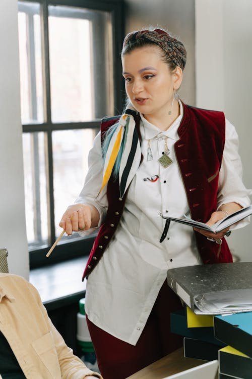 A Woman in White Long Sleeves Talking while Holding a Notebook