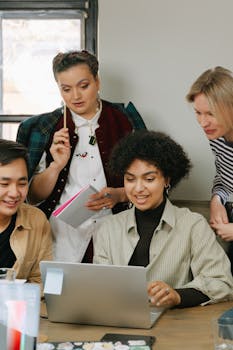 A group of diverse coworkers engaged in a collaborative business meeting using a laptop.