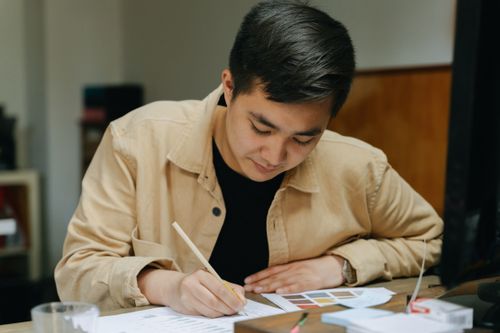 Free An adult man concentrates on writing at a desk indoors, with papers and pencils around him. Stock Photo