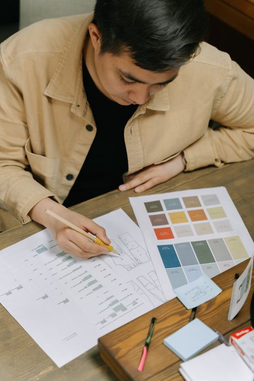Free An adult man planning a project with color palette and sketches at a wooden desk. Stock Photo