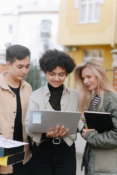 Three diverse young adults collaborating with a laptop outdoors, symbolizing teamwork and technology integration.