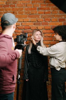 A behind-the-scenes look at a photo shoot with a diverse crew setting up in front of a brick wall.