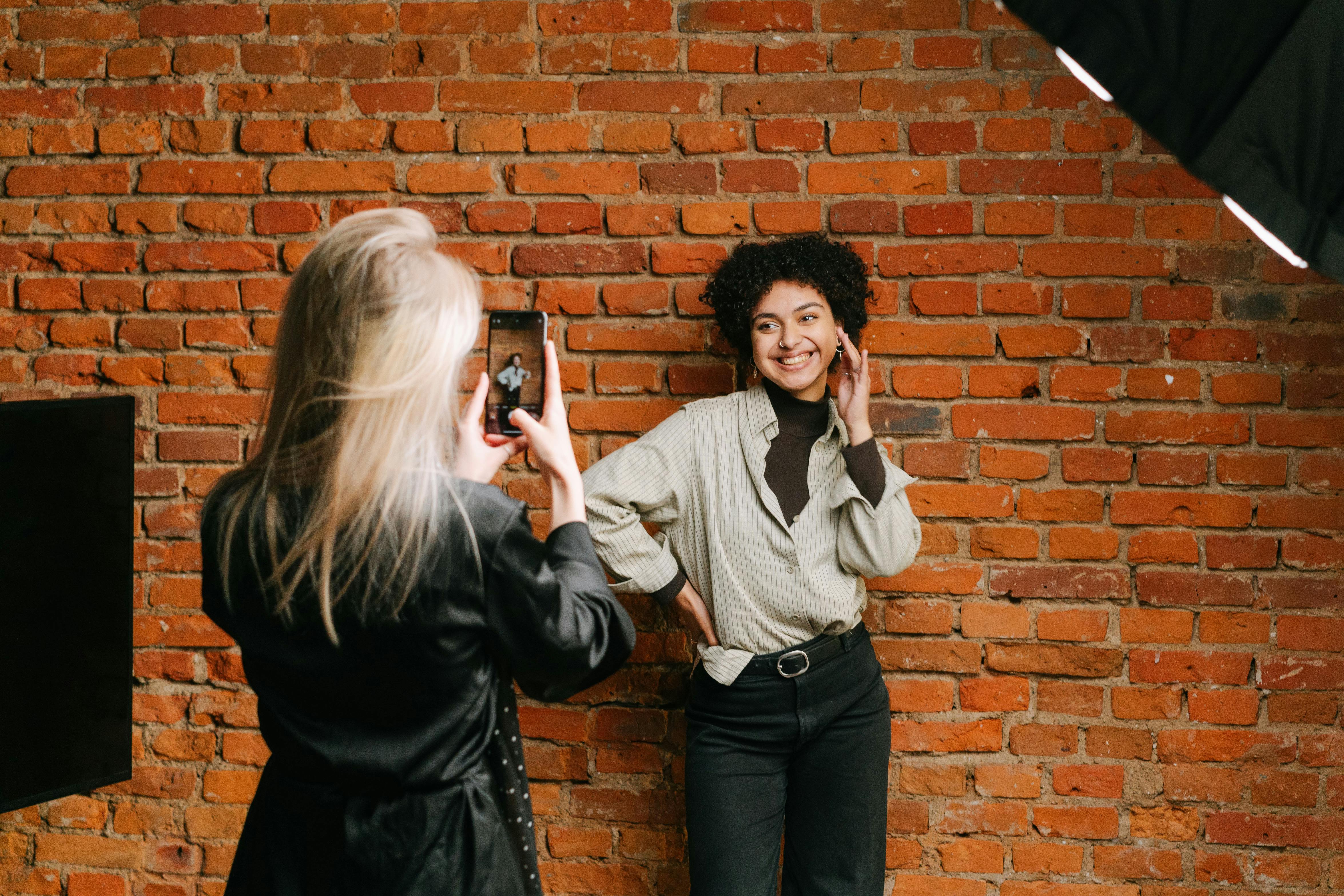 a person taking pictures of a woman posing in front of a brick wall