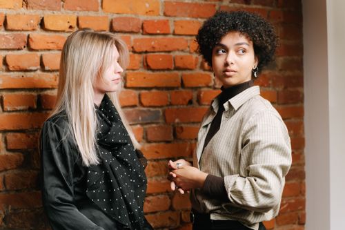 Free Two stylish women with distinct hair and attire stand by a brick wall. Stock Photo