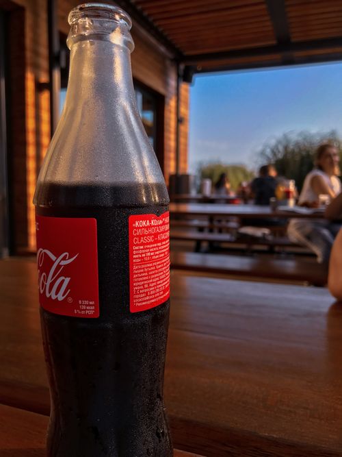 Free Close-up of a cold soda bottle on a wooden table in a sunny outdoor cafe. Stock Photo
