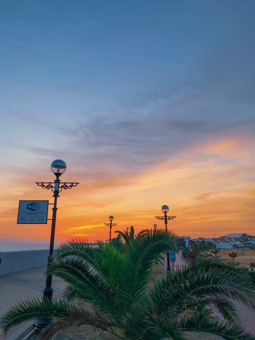 Free Beautiful sunset over a tropical beach promenade with palm trees and decorative lamp posts. Stock Photo
