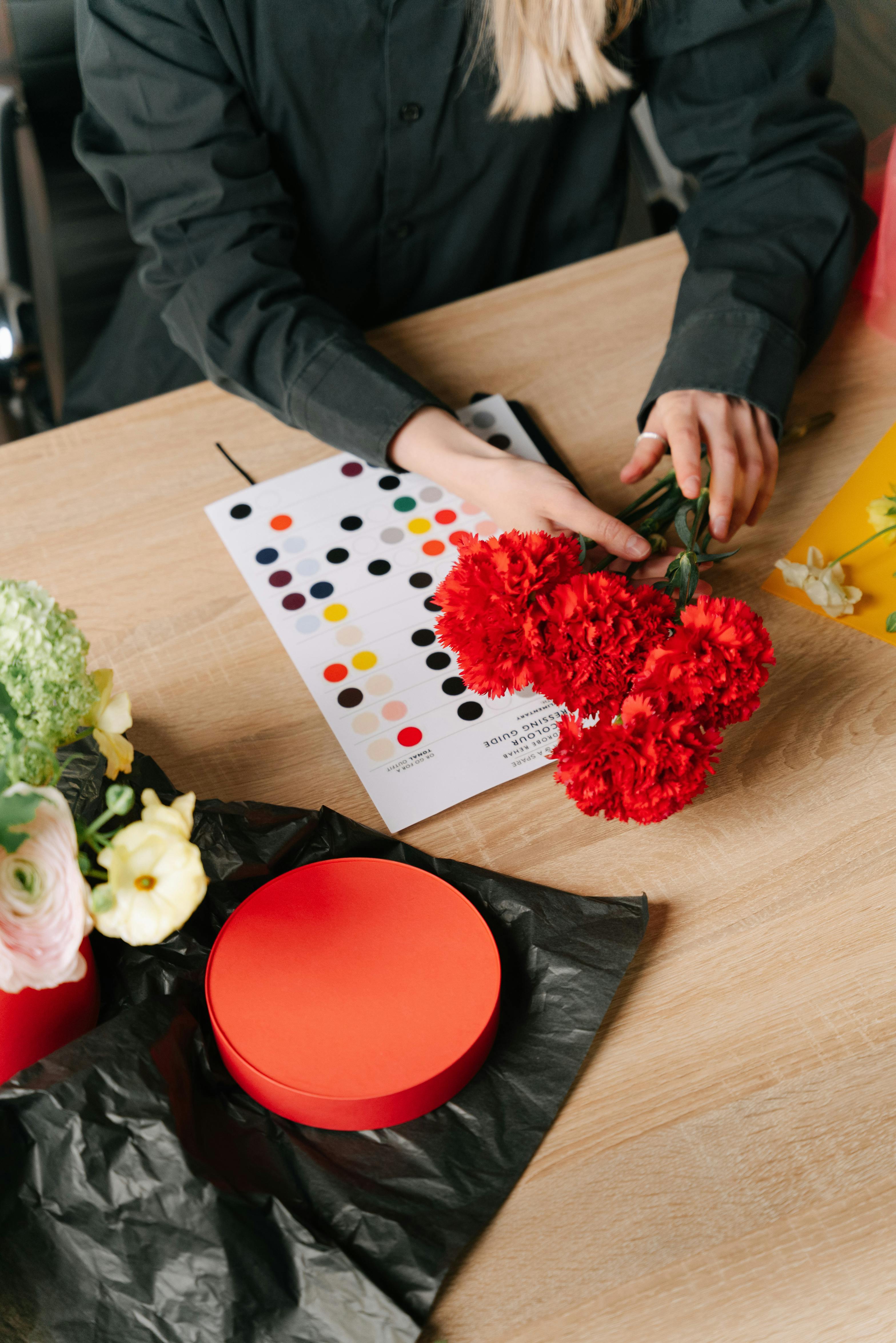 A florist arranges vibrant red carnations on a wooden table with color swatches nearby.