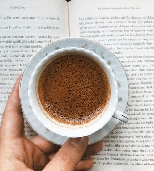 Free A hand holds a cup of Turkish coffee over an open book, creating a cozy reading atmosphere. Stock Photo