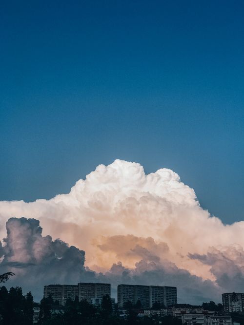 Free A cityscape under dramatic cumulus clouds and clear blue sky at dusk, showcasing tall buildings below. Stock Photo