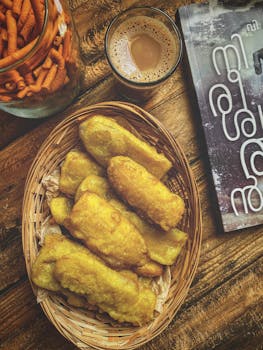 Basket of pisang goreng with coffee and crispy snacks on a wooden table.